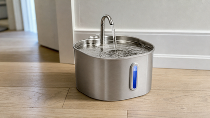Stainless steel cat water fountain running on oak flooring in a home
